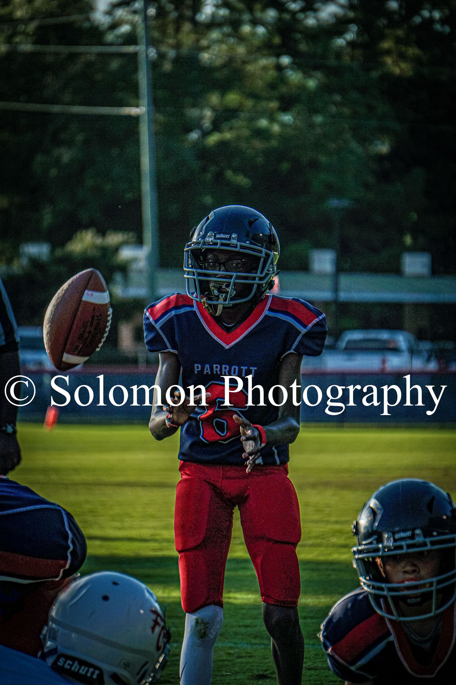 A Parrott football player in blue and red uniform catches a football during a night game.