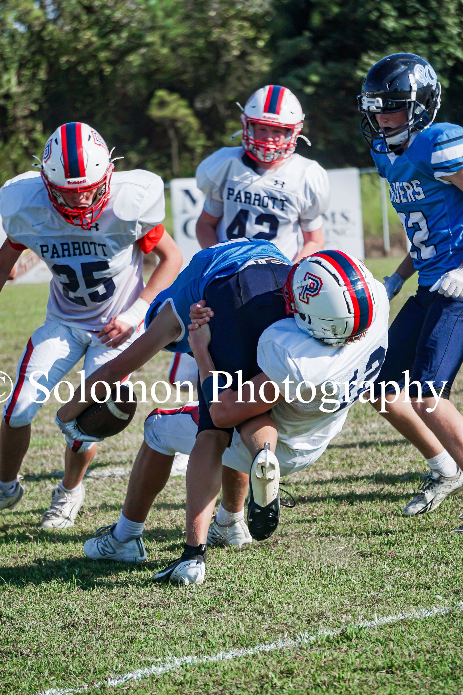 Parrott football players in white jerseys tackle an opponent during a youth football game.