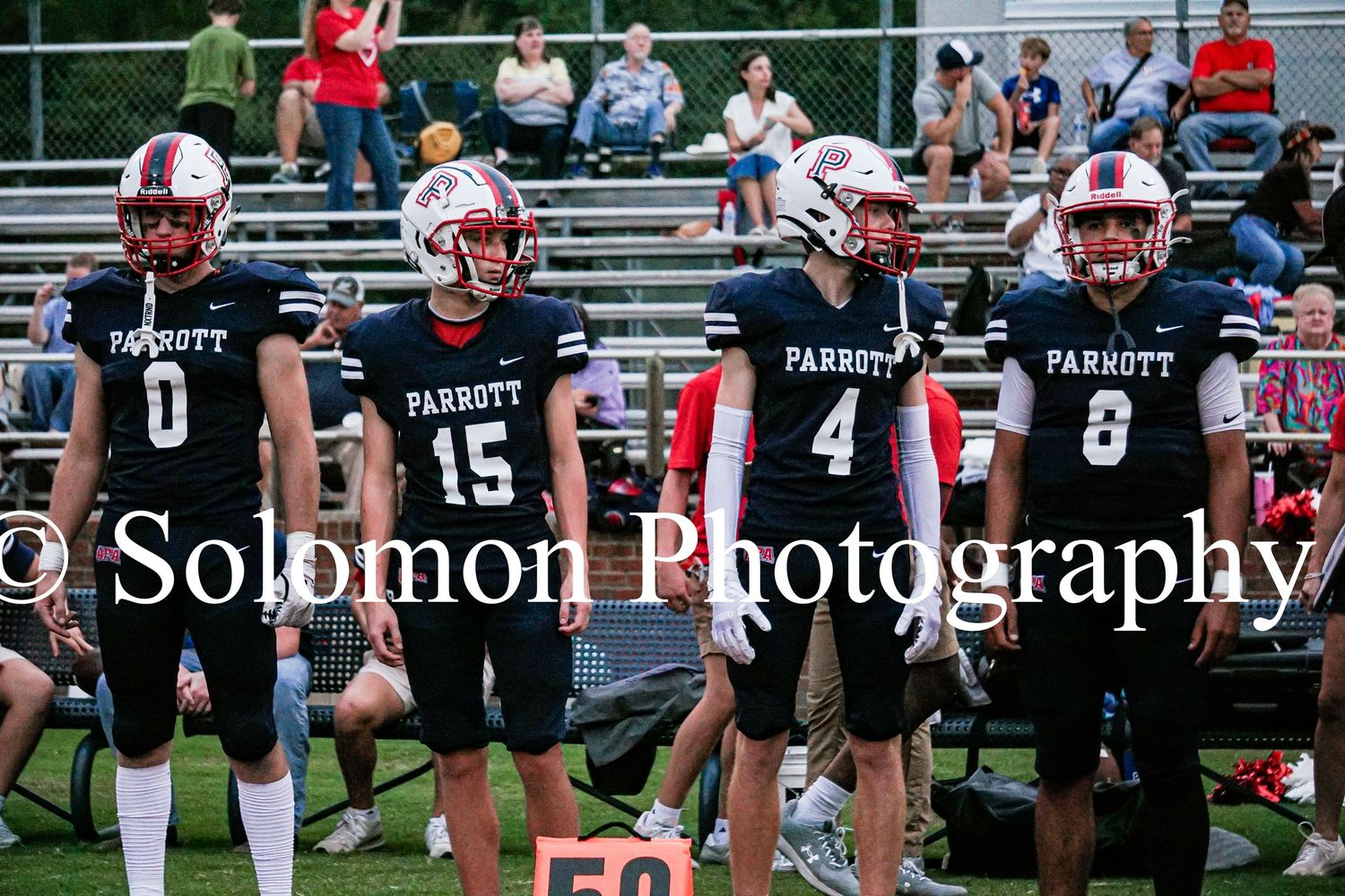 Parrott Academy football players numbers 0, 15, 4, and 8 stand together on the sideline during a game.