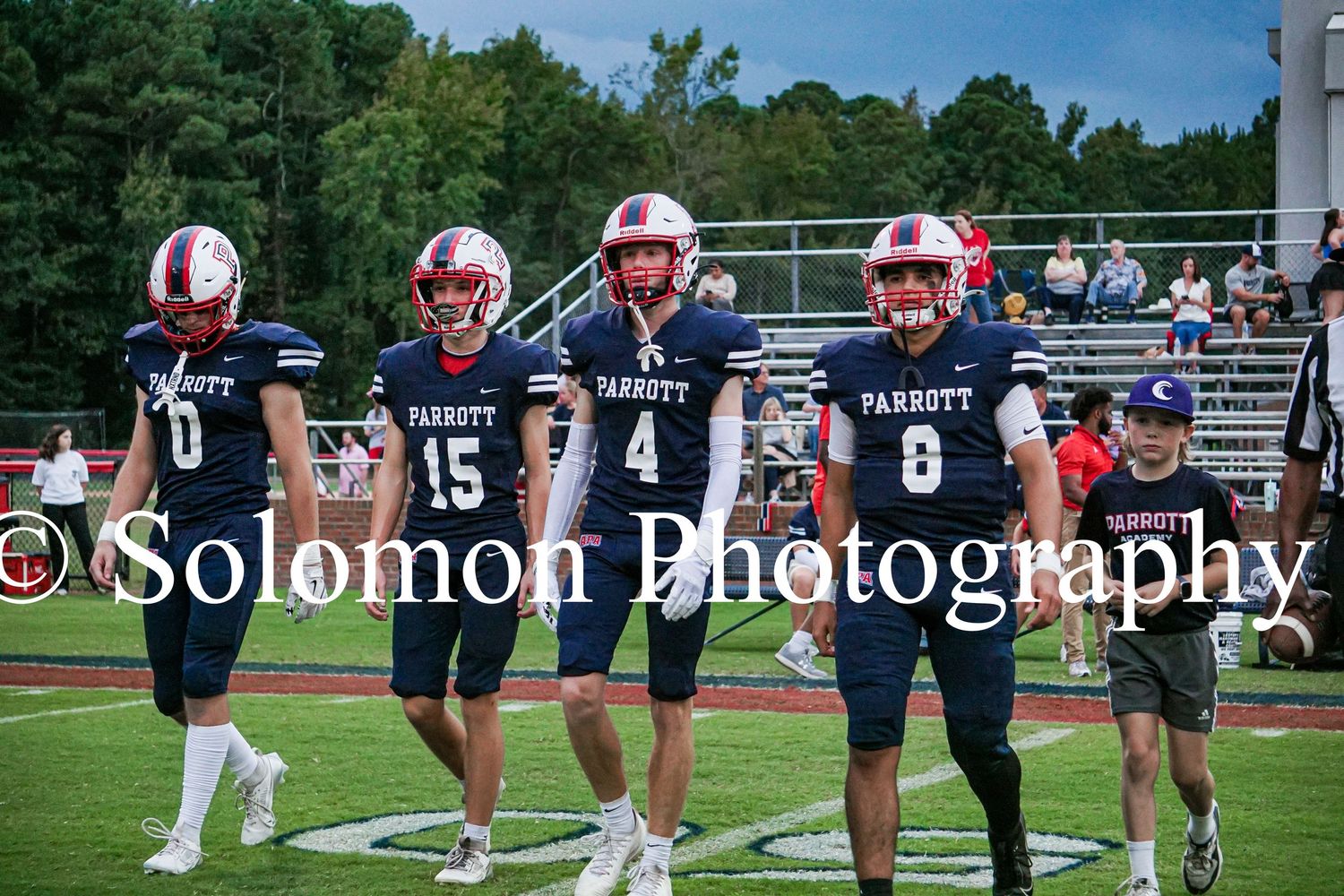 Four Parrott Academy football players in navy uniforms walk together on the field before a game.