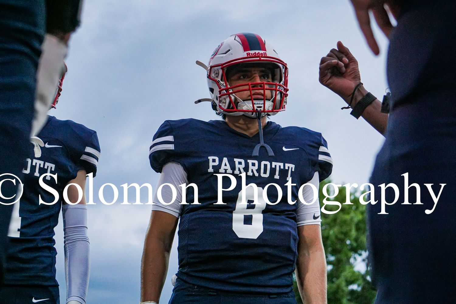 Parrott Academy football player number 8 in navy uniform listens during a team huddle on the field.