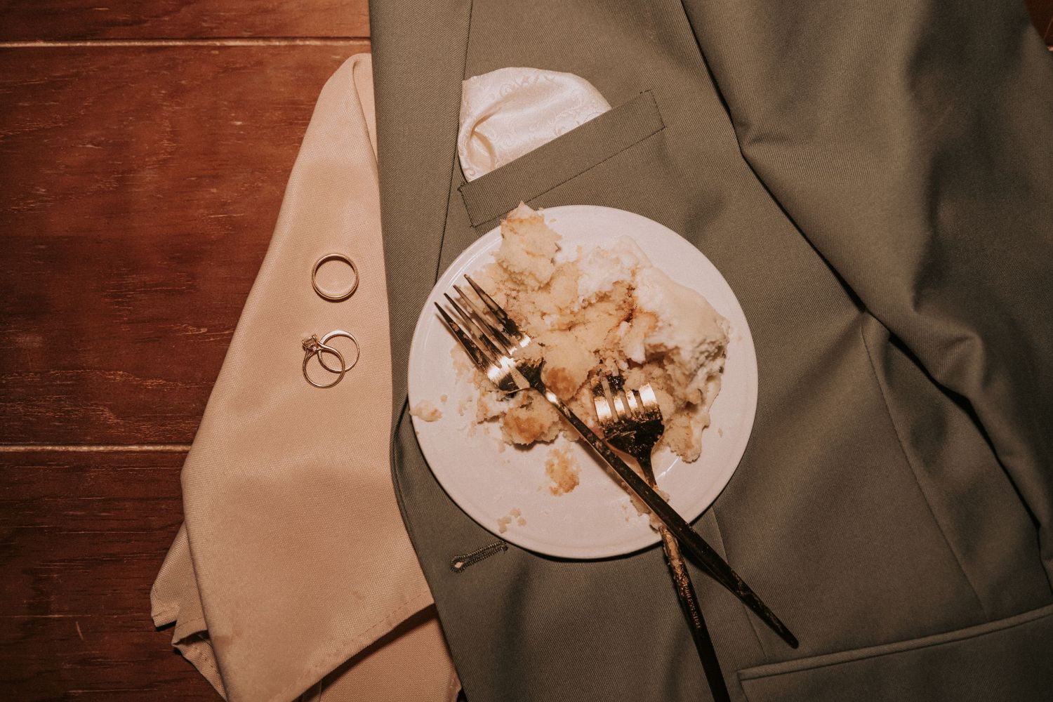 A half-eaten slice of cake with fork on a plate rests on tan and olive suit jacket against wooden surface. New Mexico wedding photographer