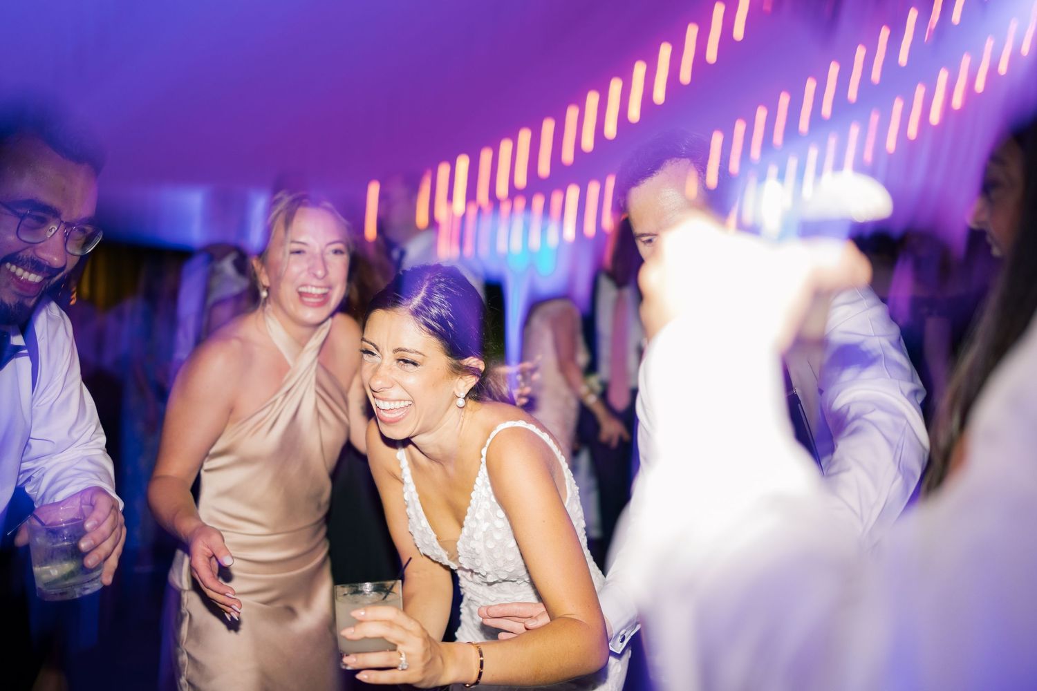 People enjoying a lively nightclub party with purple lighting and drinks in hand.