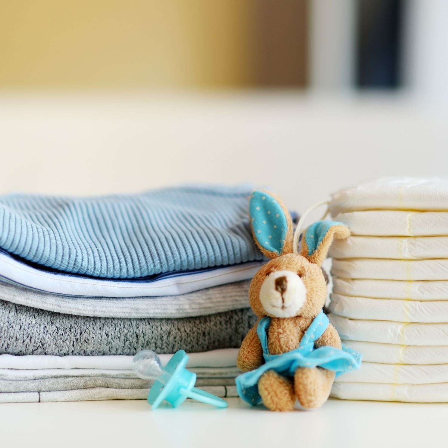 Baby blankets in blue and gray tones, pile of baby diapers, a brown staff bunny with some blue details and a blue pacifier.