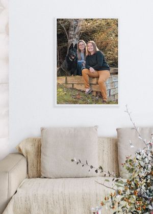 A framed family photo displayed on a cream-colored living room wall above a beige couch with decorative flowers nearby.