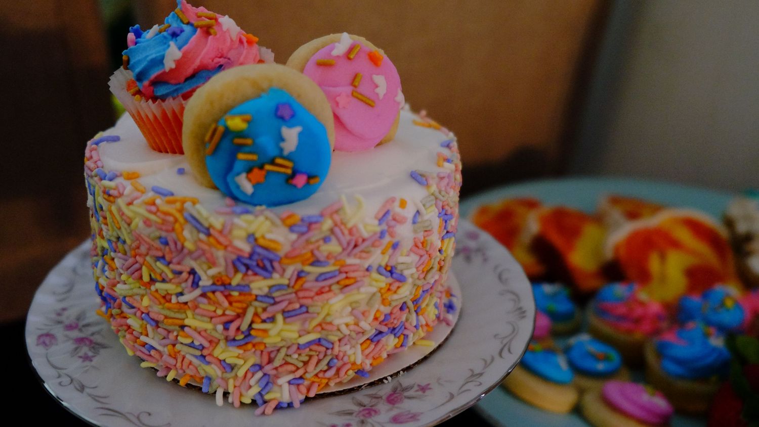 A colorful cake decorated with sprinkles and topped with vibrant blue and pink donuts sits on a white plate.