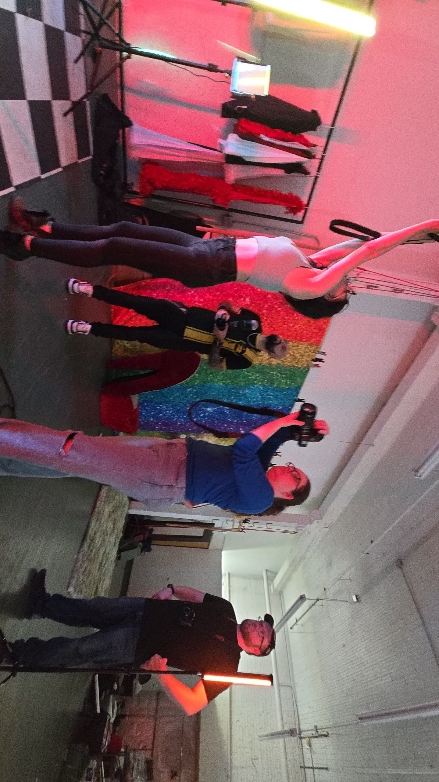 Colorful retail clothing display featuring a sparkly rainbow sequined garment and various outfits under pink lighting.