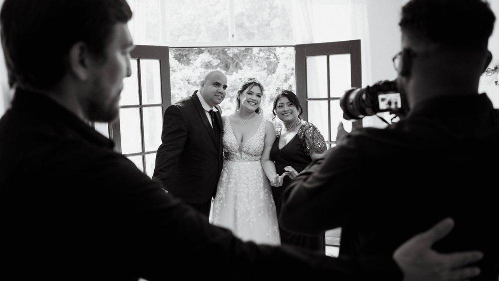 Silhouettes of wedding guests hug and embrace during an emotional reception moment in front of bright windows.