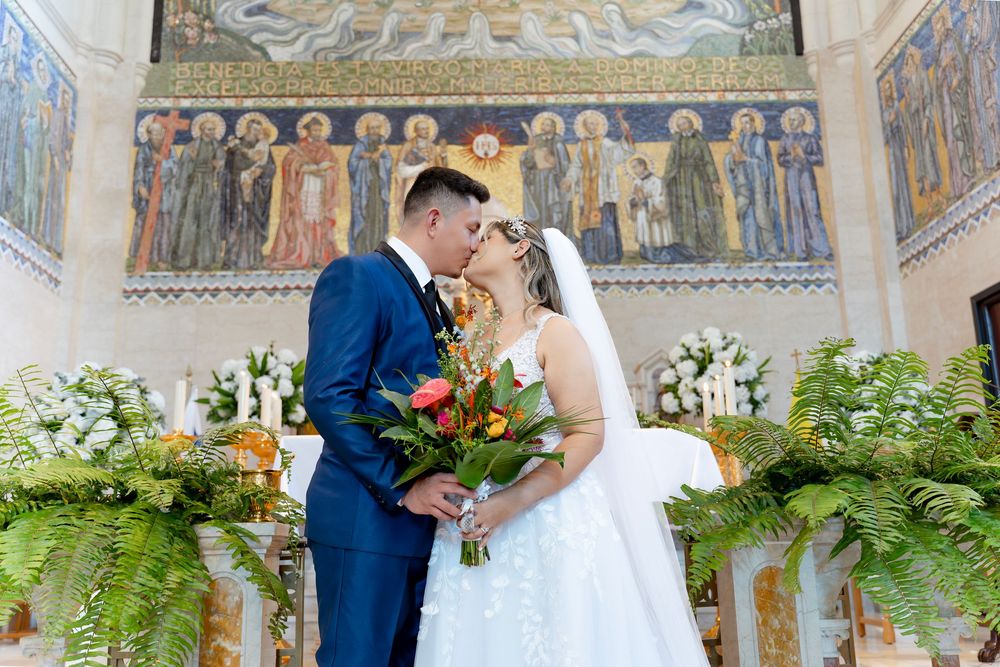A bride and groom embrace inside a historic church with ornate religious frescoes and floral decor.