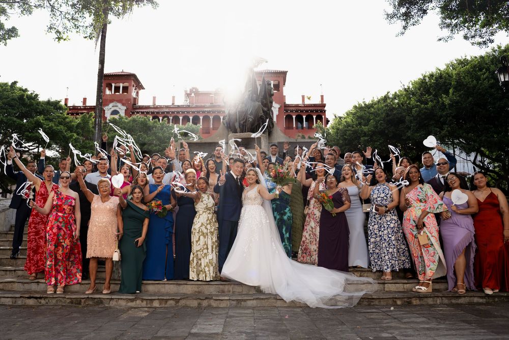Wedding guests gather on rustic stone steps to celebrate as newlyweds share a joyful moment during sunset.