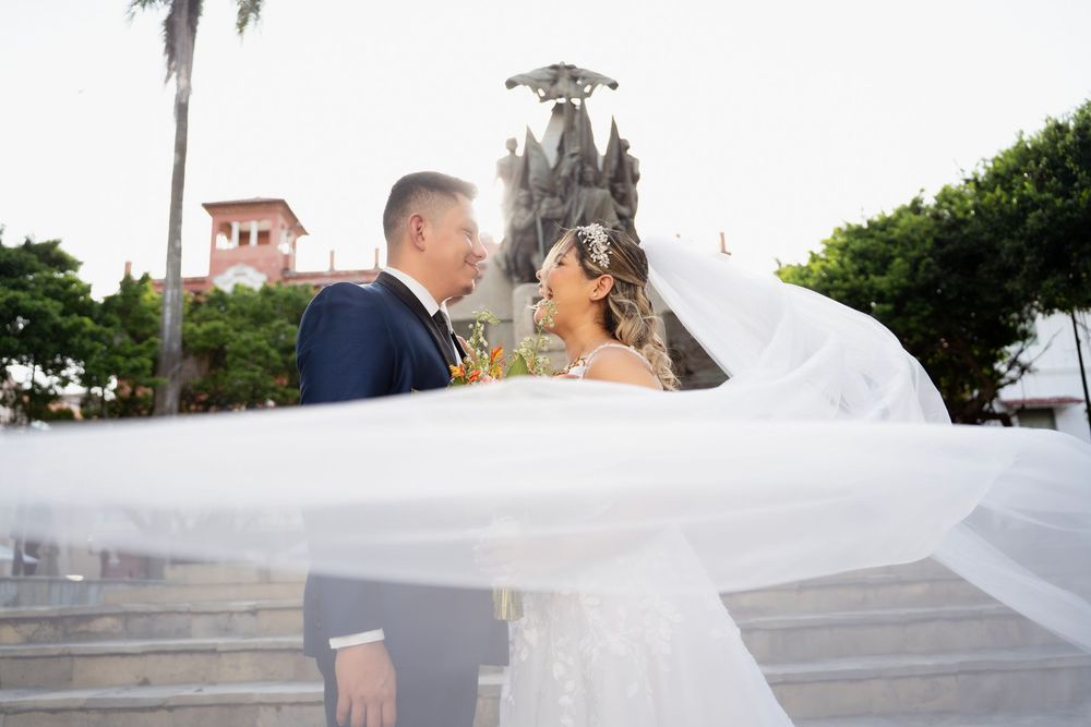 A bride and groom share a romantic moment outdoors with palm trees and coastal scenery in the background.