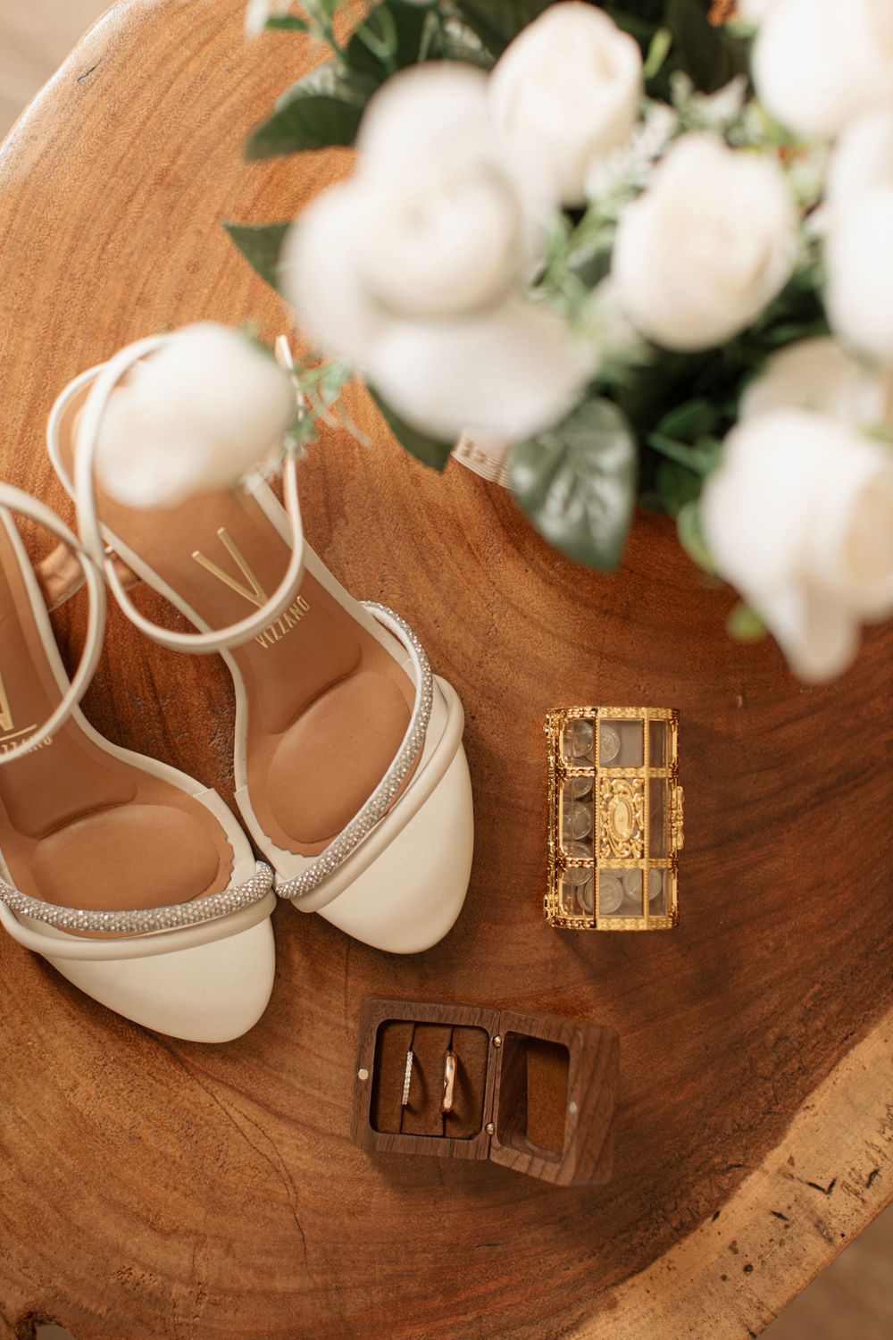 A gold jewelry box on an ornate wooden board with delicate white roses in the background.