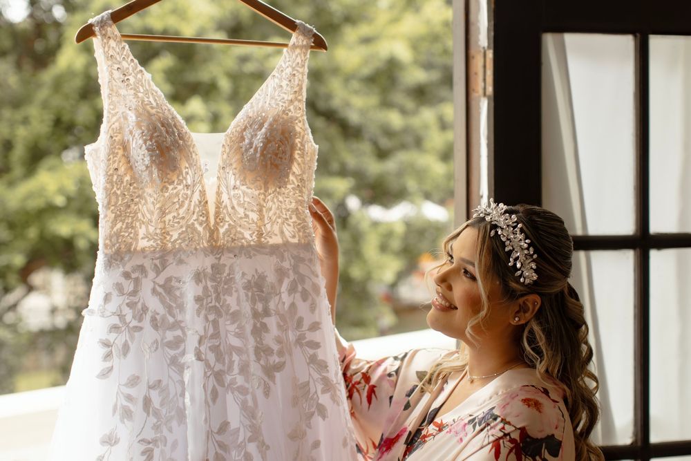 A white lace wedding dress hangs elegantly by a sunny window creating a romantic silhouette.