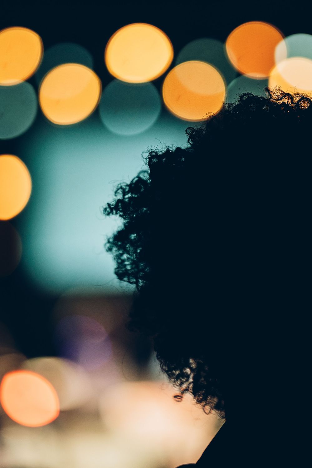Silhouette of curly hair against blurred bokeh lights creating a dreamy nighttime atmosphere.