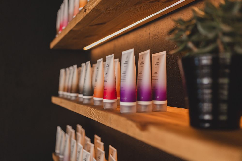 Close-up of wooden salon shelf with gradient hair care product tubes and a potted plant.