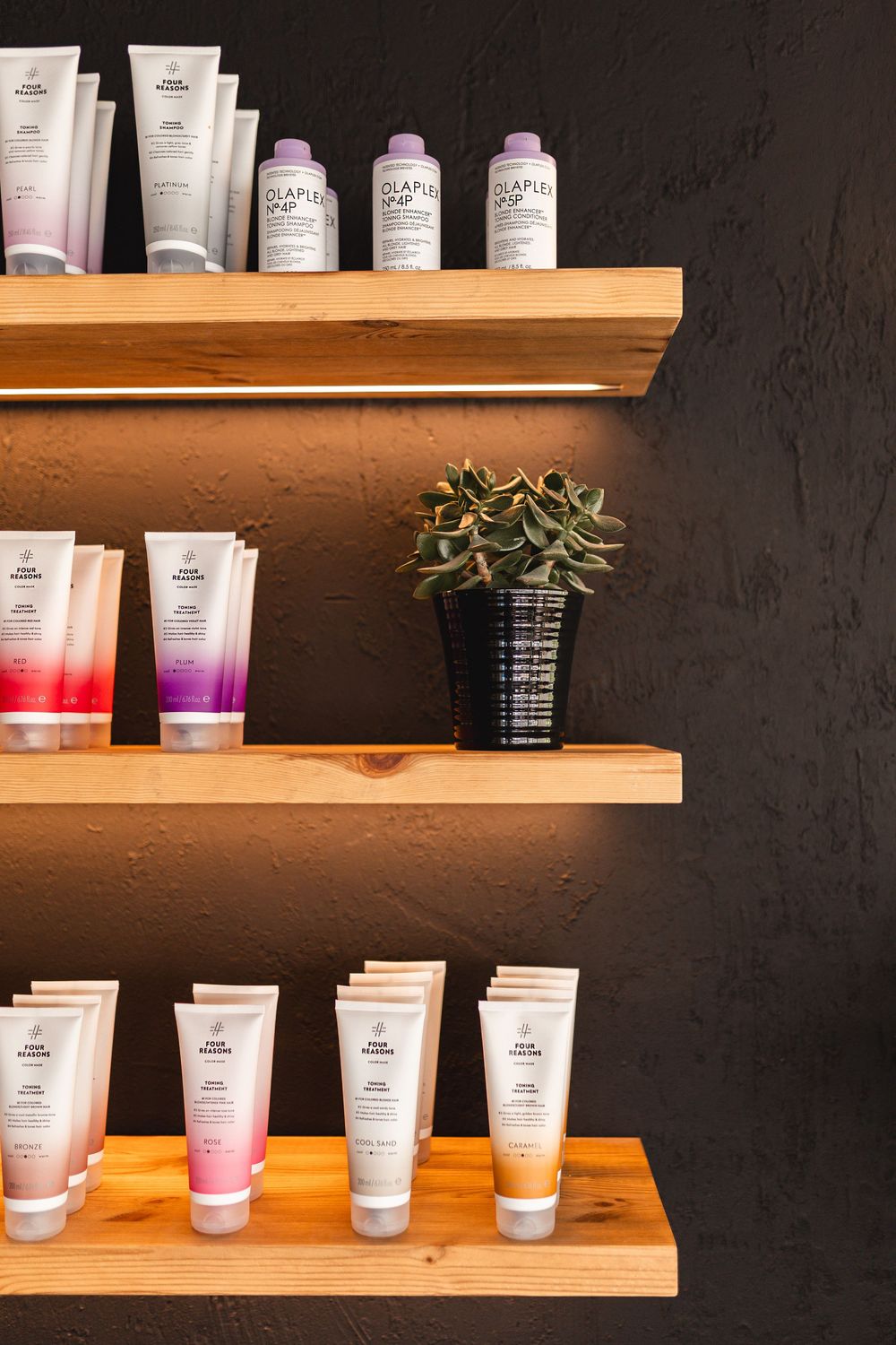 Wooden shelves displaying Olaplex and color hair care products with a small succulent plant.