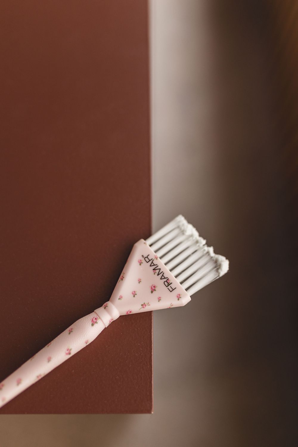 Pink Framar hair dye brush with floral design resting on a brown surface.