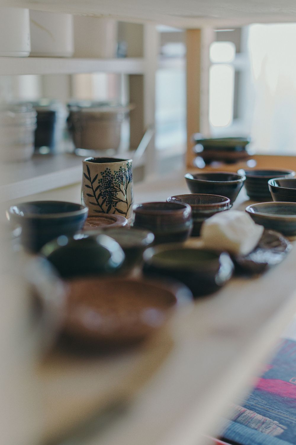 Assorted handmade ceramic bowls and a floral-patterned mug displayed on a white wooden shelf.
