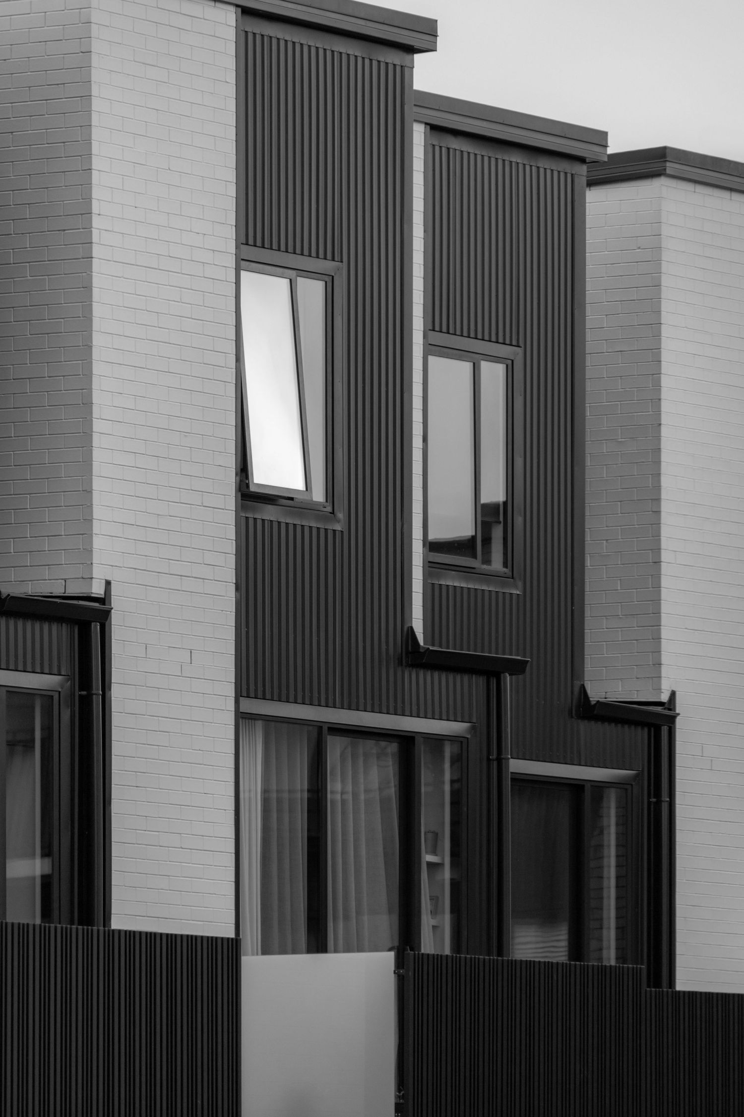 Crisp monochrome townhouse facade with vertical ribbed cladding and stark contrast between light and dark forms.