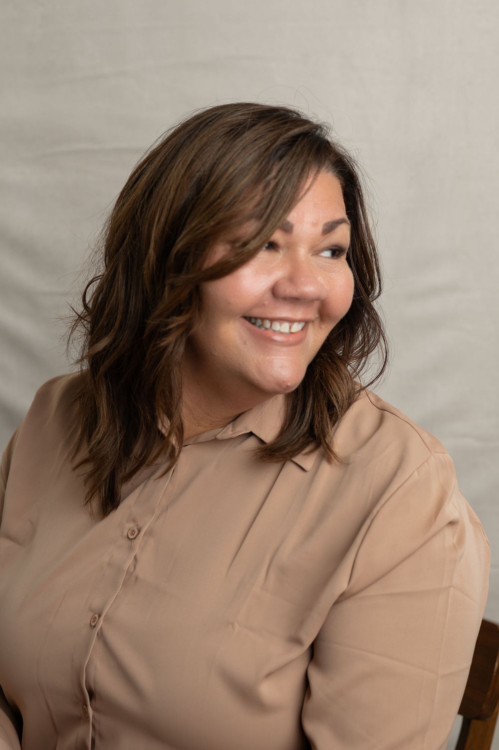 Professional portrait of someone wearing a beige button-up shirt, smiling warmly while posing against a neutral backdrop.