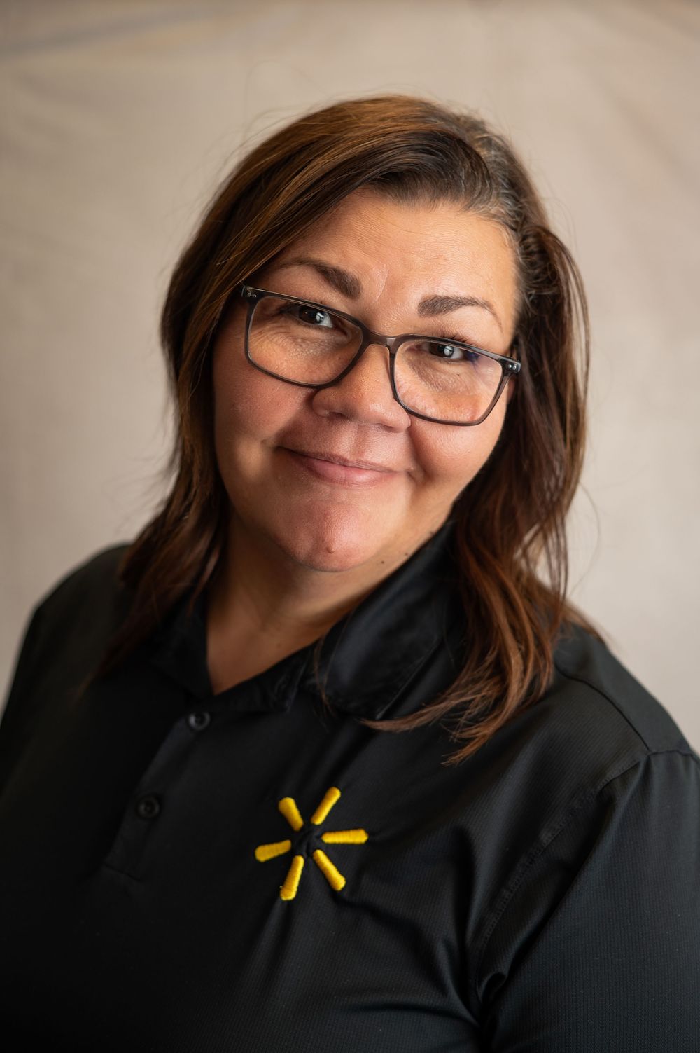 Person wearing glasses and black hoodie with yellow Walmart logo smiles warmly at camera.