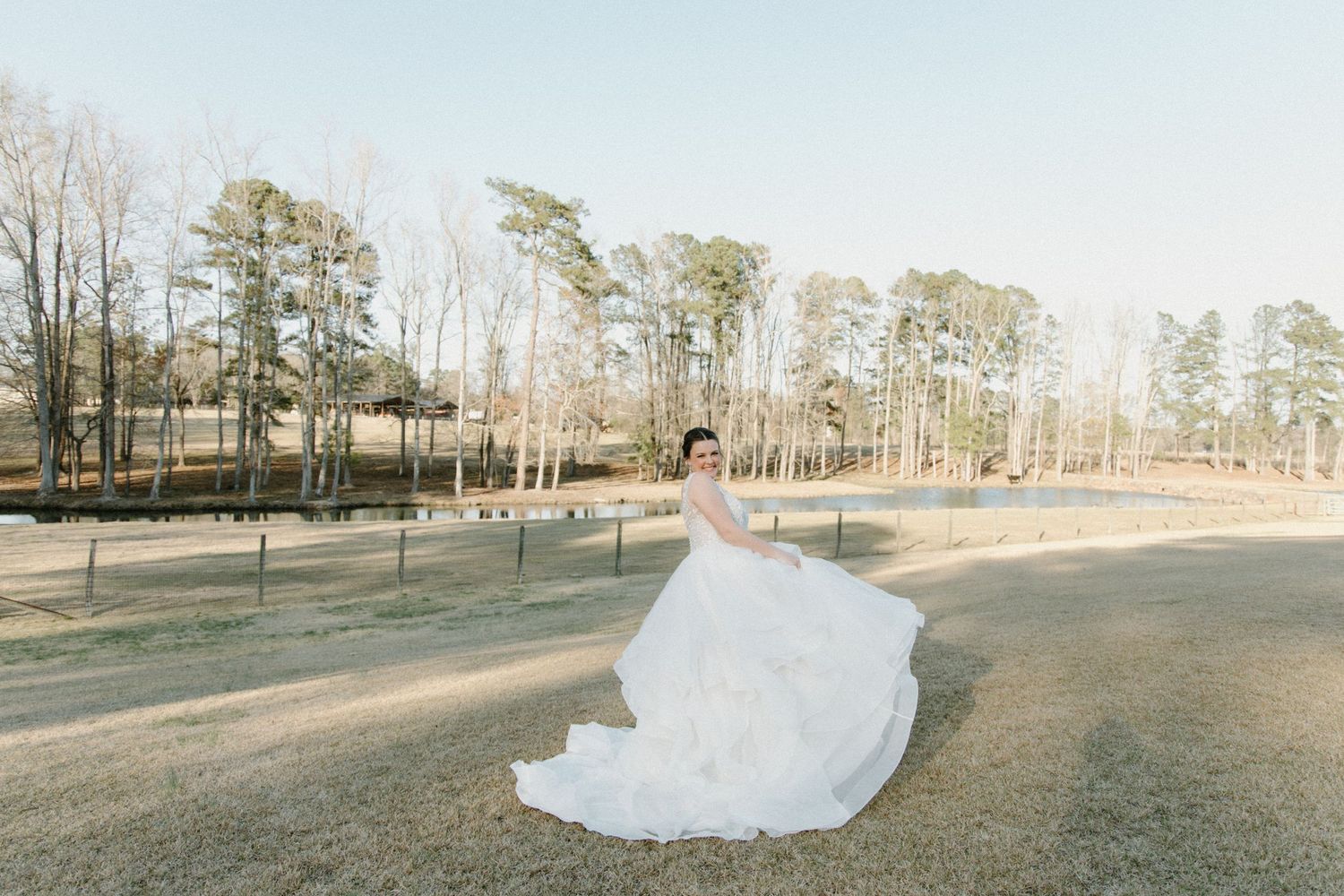 A flowing white wedding dress fills the frame as it spreads across a rustic outdoor setting with tall pine trees in winter.
