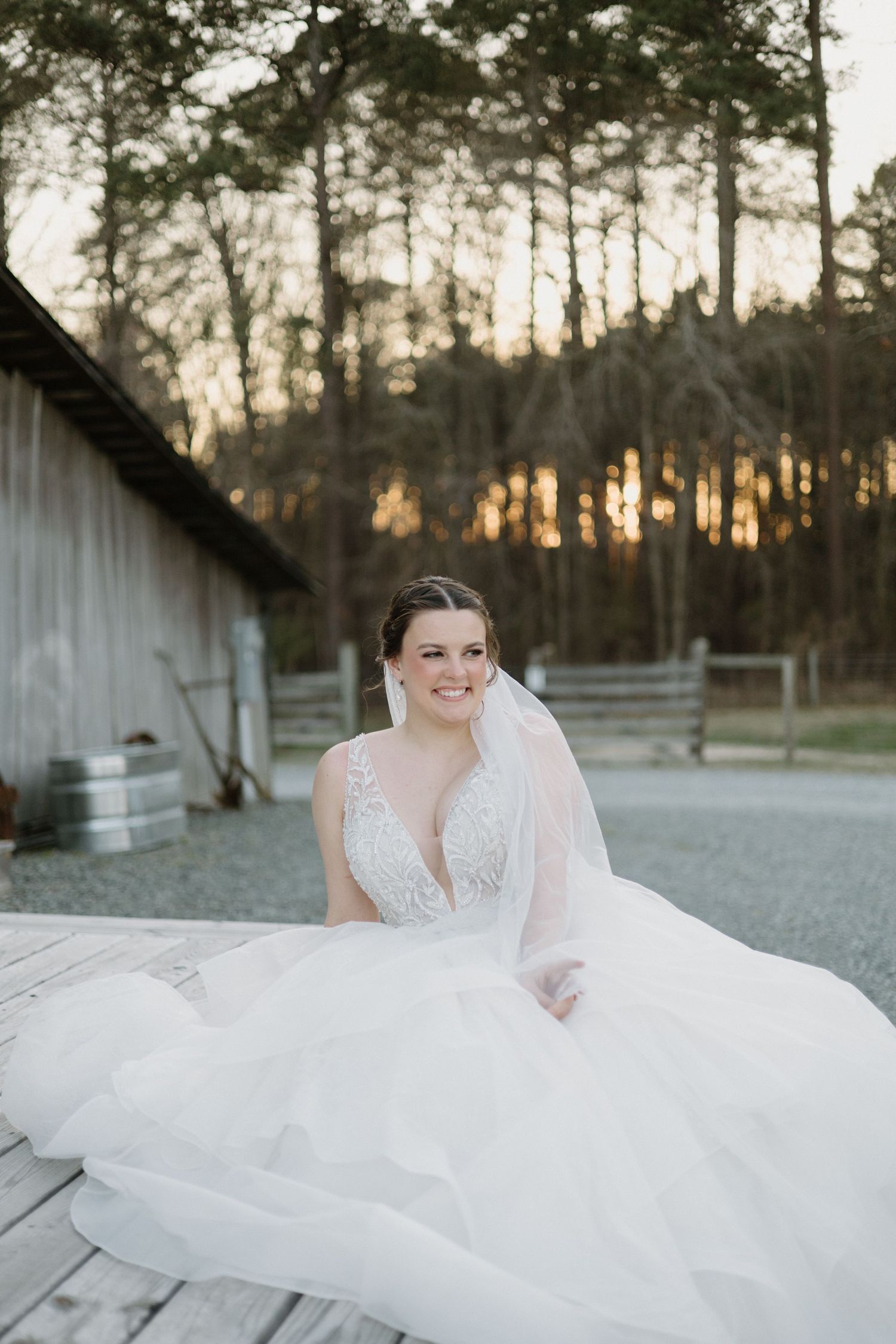 A flowing white wedding dress with delicate lace details twirls gracefully against a rustic woodland backdrop at sunset.