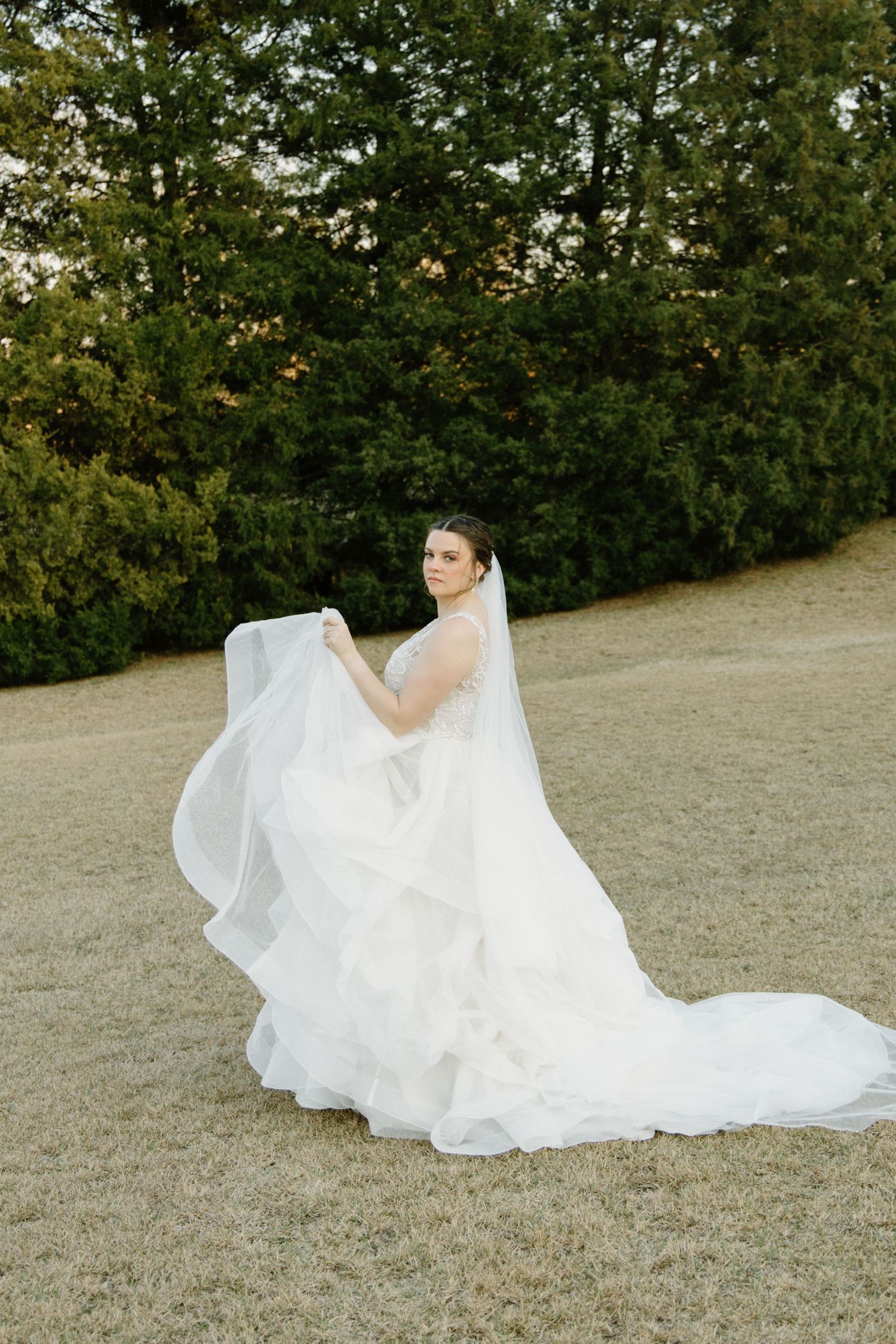 A flowing white wedding dress creates a romantic cascade effect as it drapes elegantly across a grassy outdoor setting.