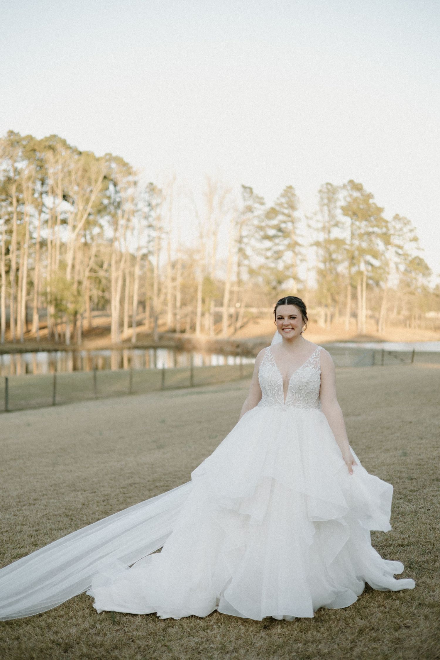 Elegant wedding dress with layered tulle skirt and deep V neckline photographed at sunset among tall trees.