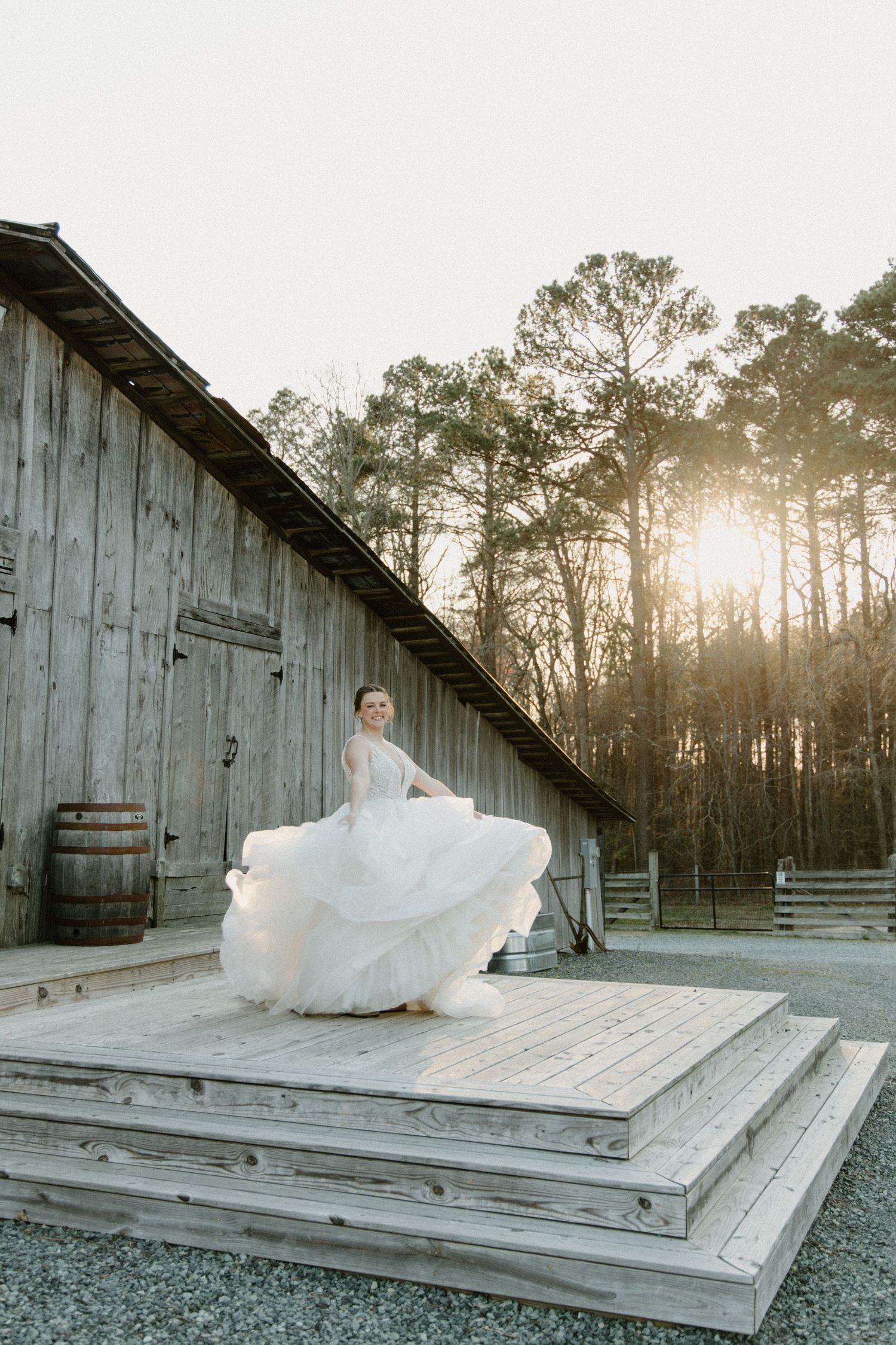 A flowing white dress billows gracefully on a rustic wooden deck surrounded by tall pine trees at sunset.
