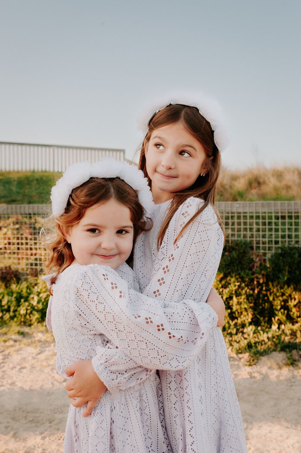 Children in matching white lace dresses embrace on a beach during sunset, creating a tender candid moment.
Altona Family Photographer