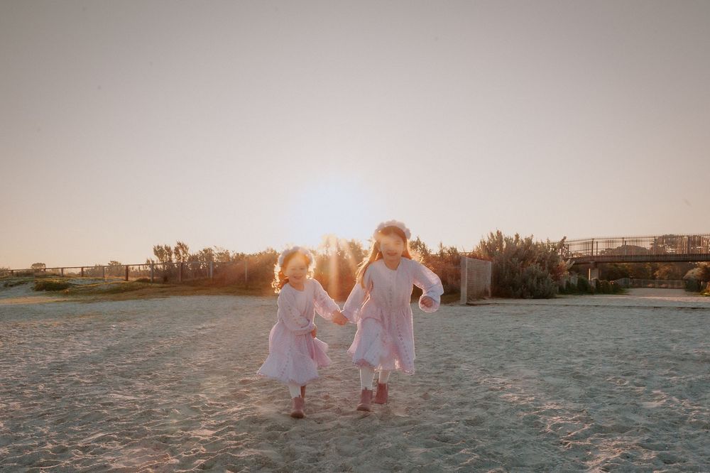 A group wearing white dresses walks along the beach shoreline at dusk with golden light illuminating the scene.
Altona Family Photographer