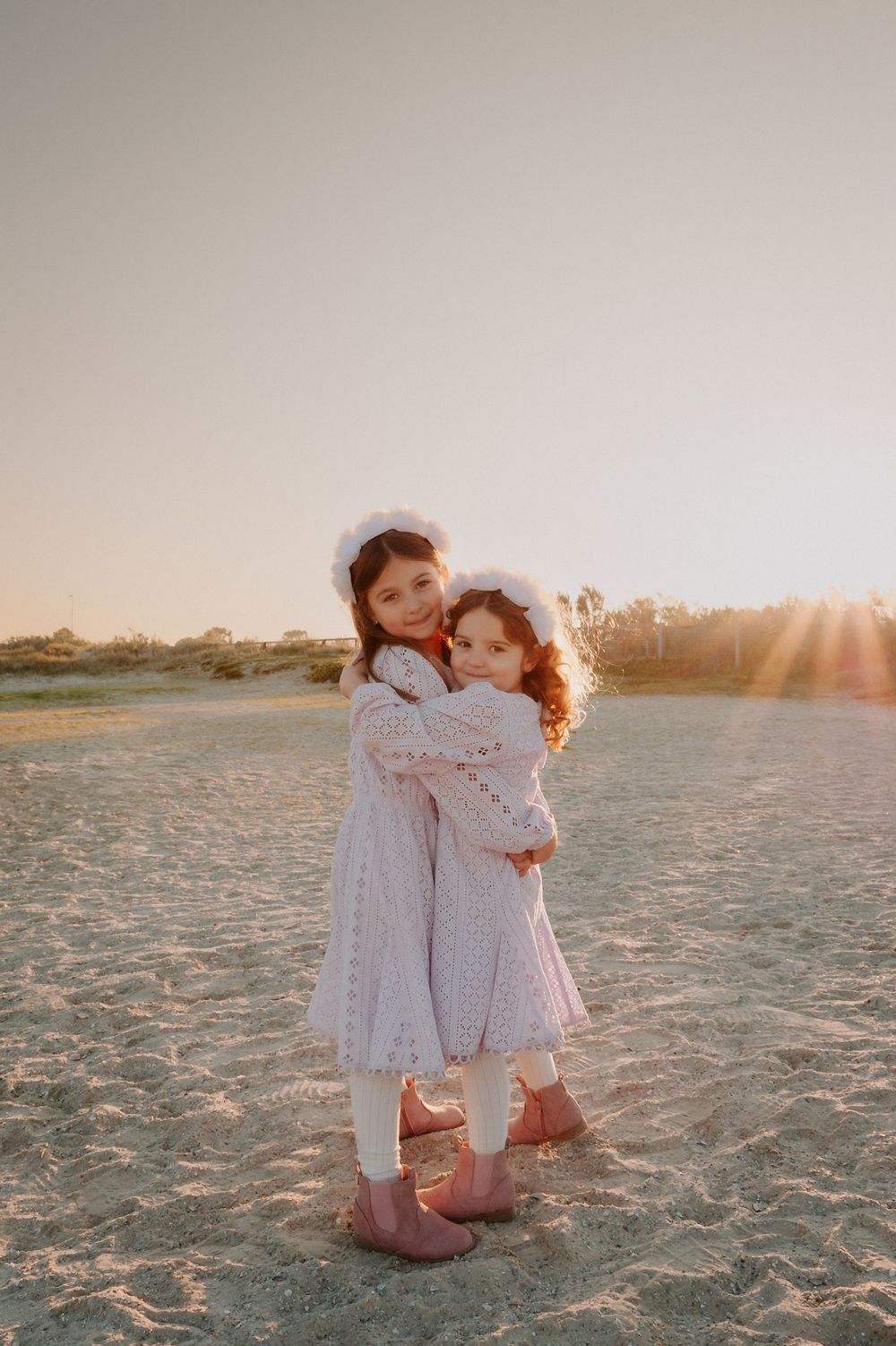 Two young children in white outfits share a sweet embrace while standing on a beach during golden hour sunset.
Altona Family Photographer