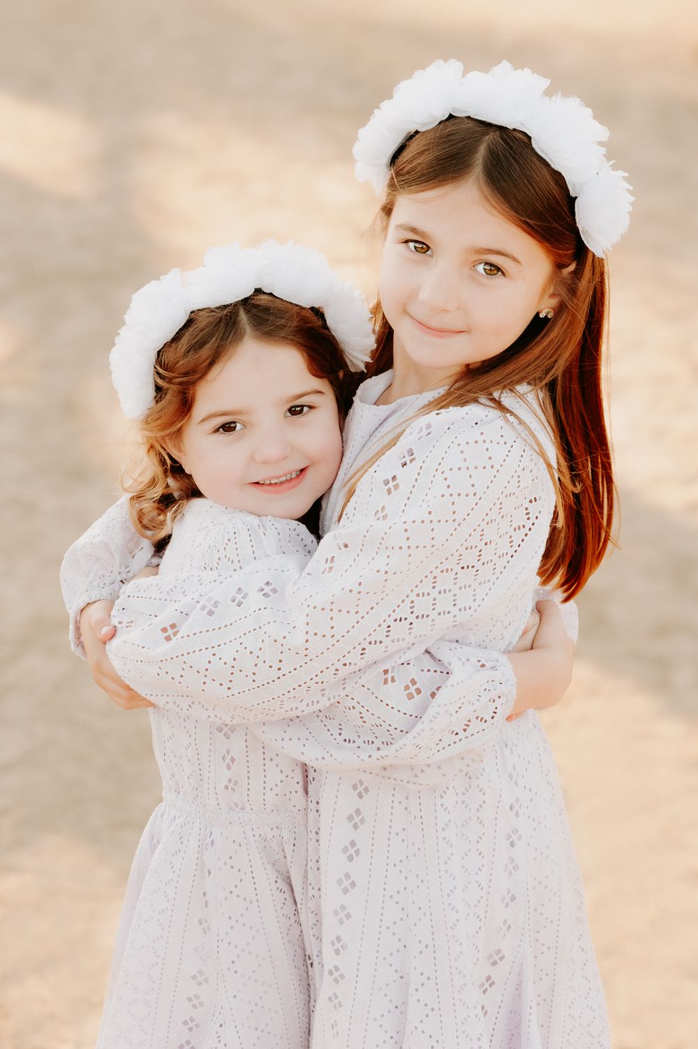 Two children wearing matching white lace dresses and white hair accessories stand together in soft lighting.
Altona Family Photographer