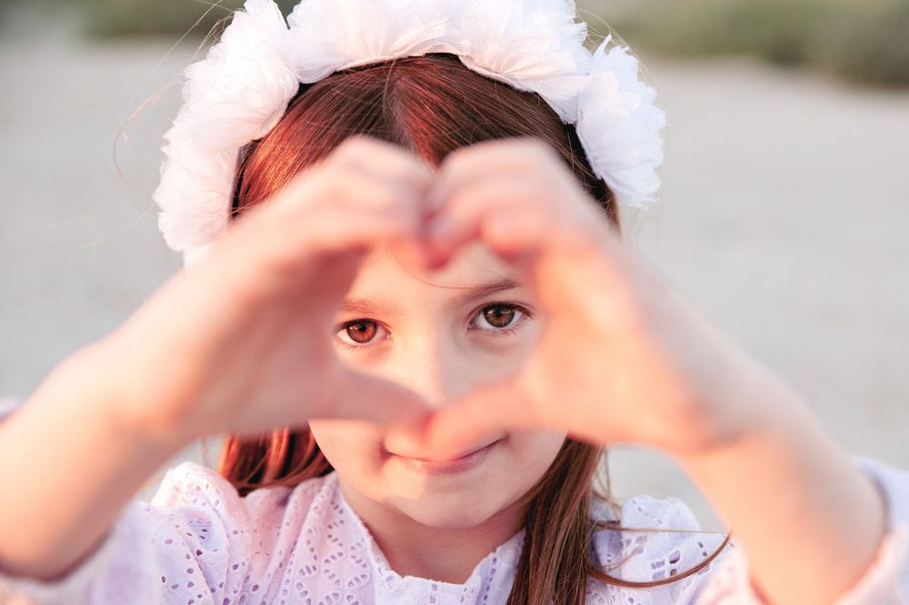 A child makes a heart shape with their hands while wearing a white lace dress and headband.
Altona Family Photographer Melbourne