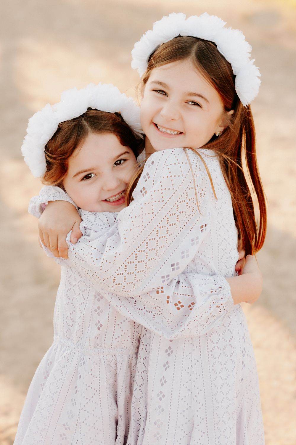 Two children in white lace dresses share tender hugs and smiles against a soft sunset backdrop.
Altona Family Photographer Melbourne
