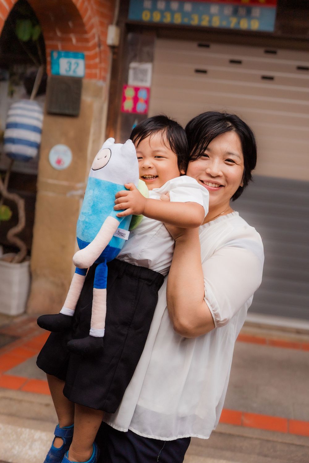 A joyful moment captured outdoors with a blue plush toy in front of a brick building.