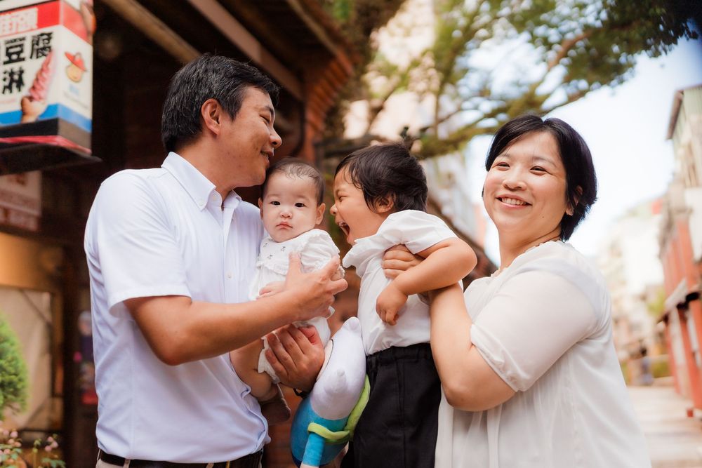 A joyful family moment captured outdoors with a small child being lifted up in a playful interaction.