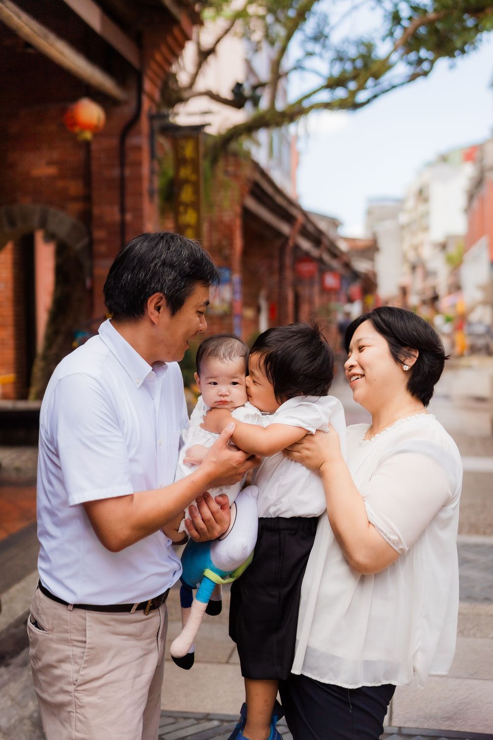 A family shares a joyful moment together on a traditional brick-lined street with red lanterns.
