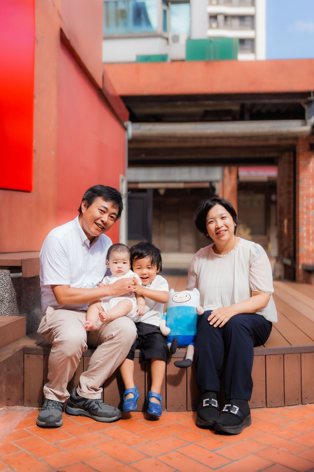 A family sits together on red brick steps outside a modern building in an urban setting.