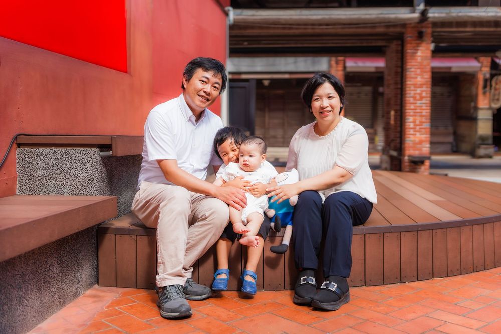 A family sits together on red brick steps outside a traditional building on a sunny day.