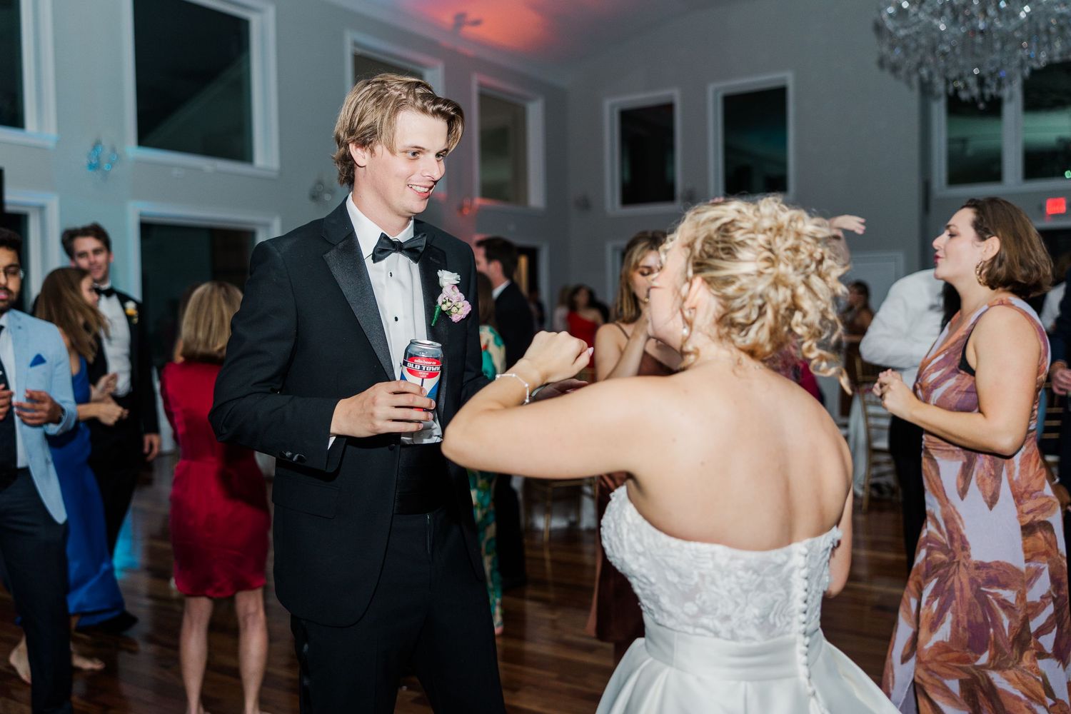 Wedding reception guests mingle and dance in an elegant venue with large windows.