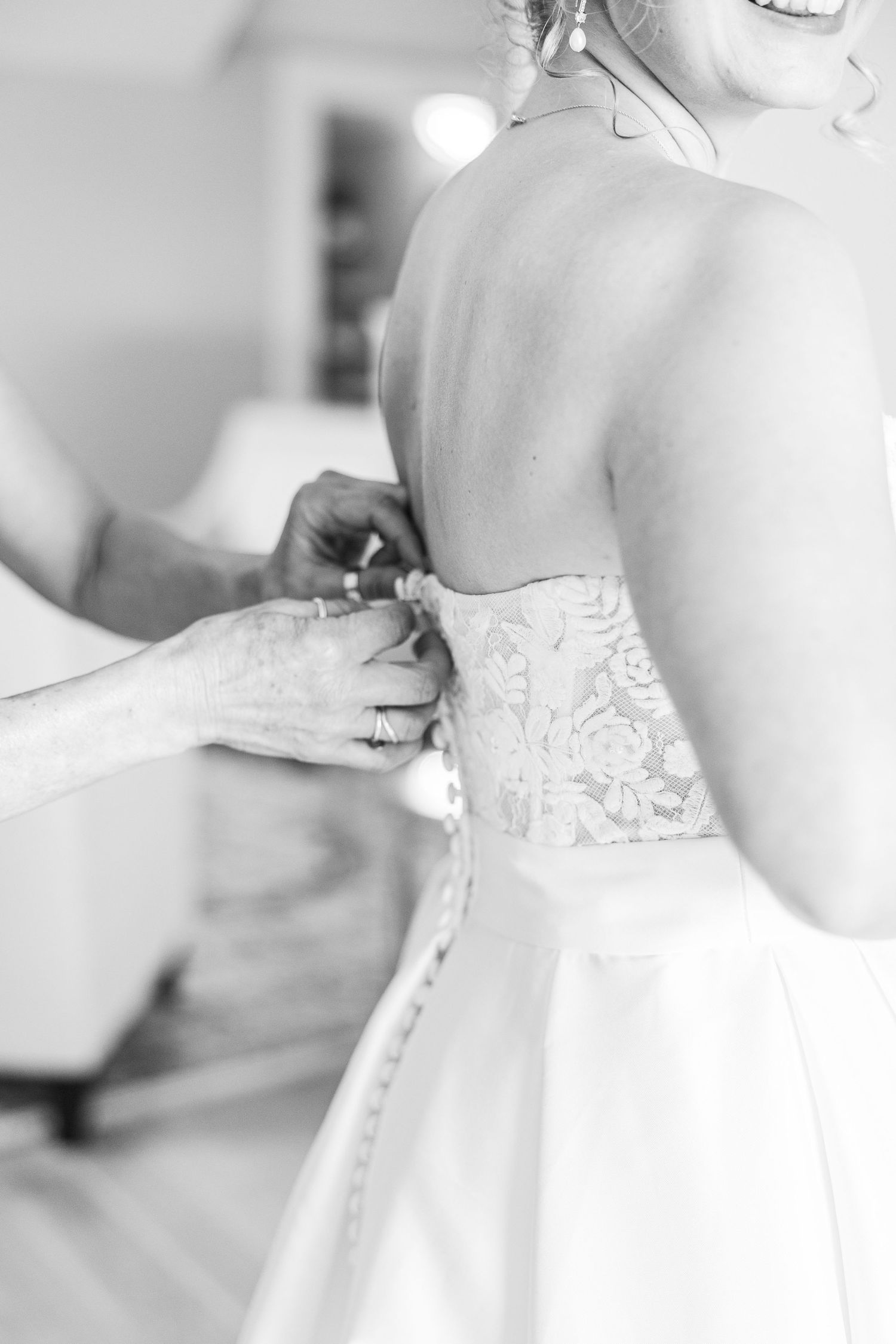 Black and white photo of someone helping to button up a detailed wedding dress.