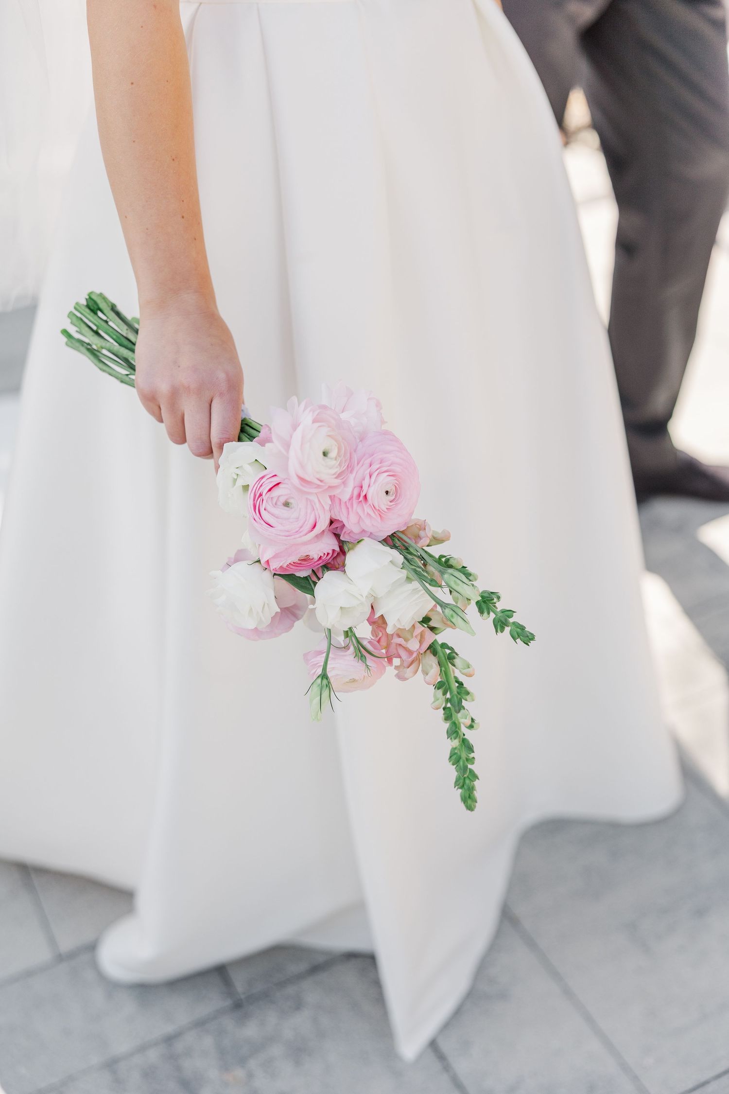 A delicate pink and white wedding bouquet held against a flowing white wedding dress.