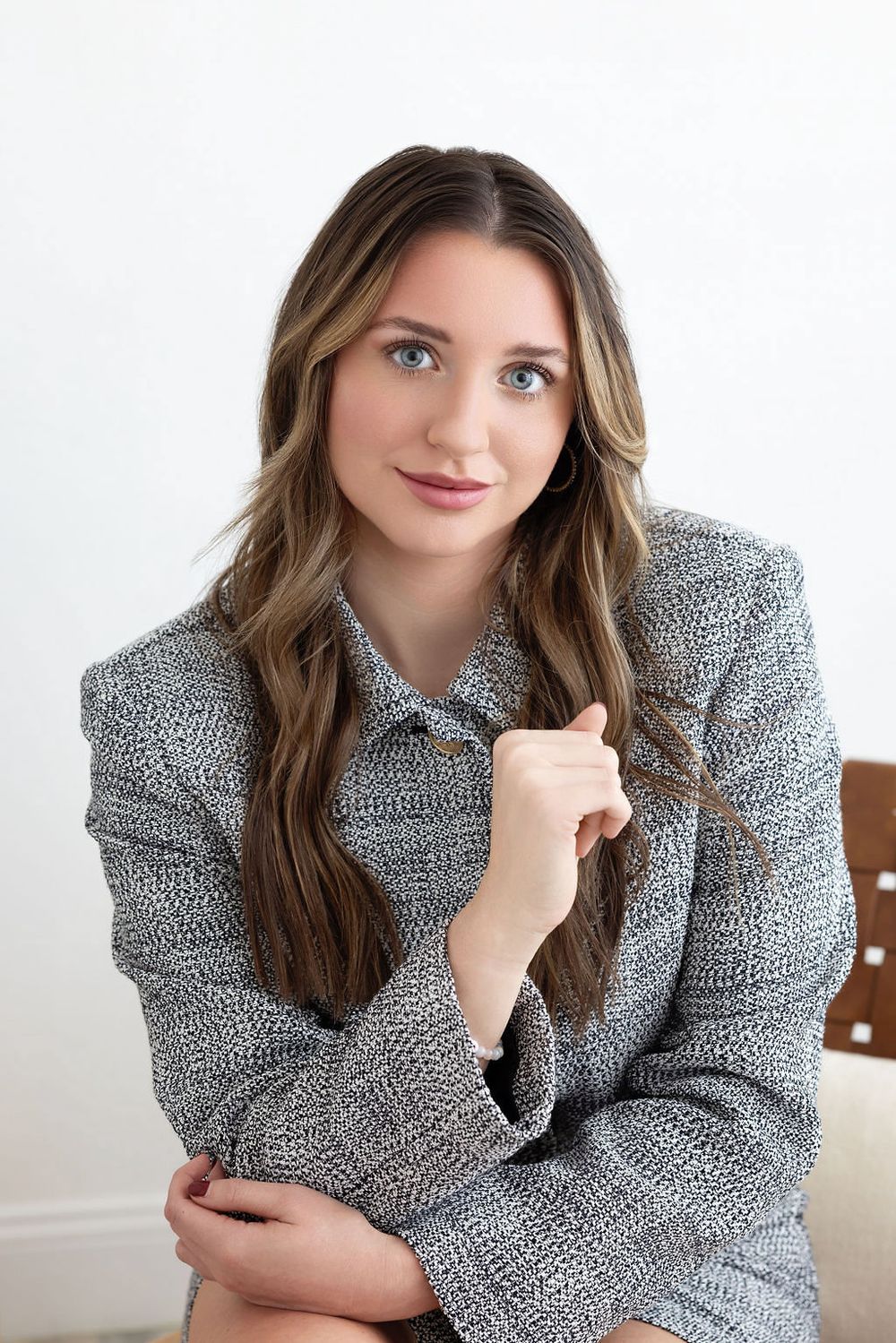 Professional portrait of a person in a textured gray blazer sitting against a white wall.
