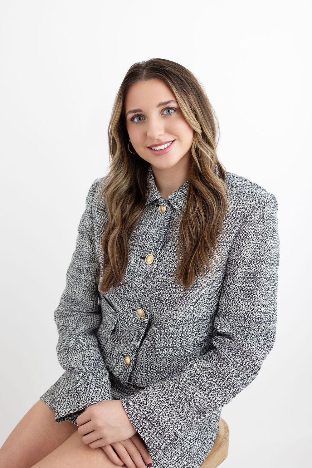 Professional portrait against white background wearing gray plaid blazer with gold buttons.