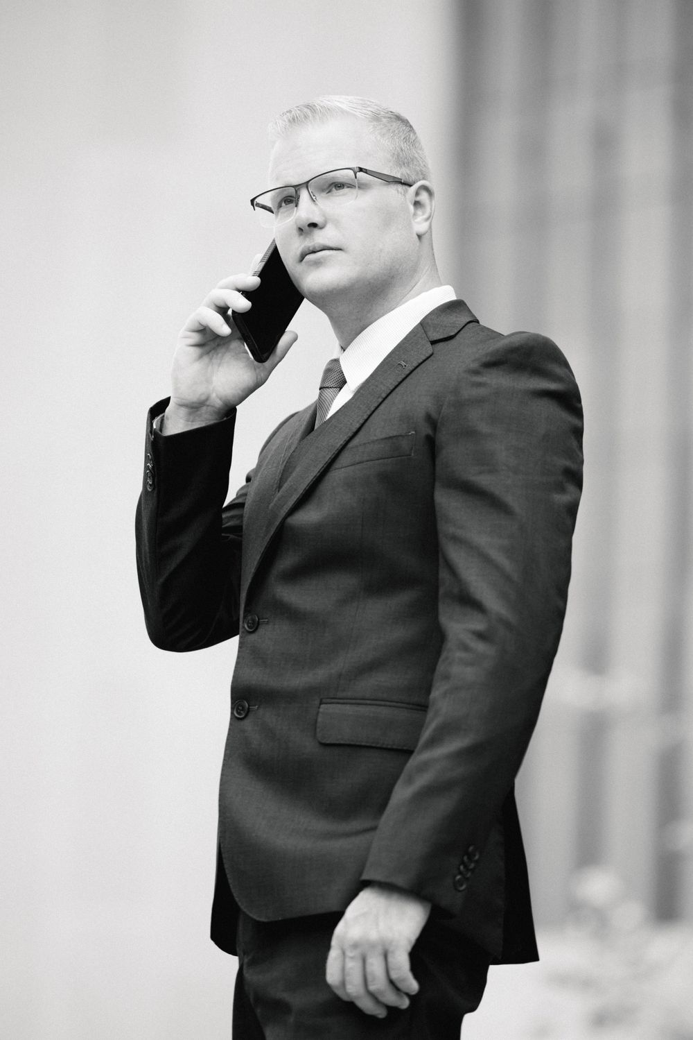 Professional in a dark suit stands thoughtfully with hand raised to chin in black and white portrait.