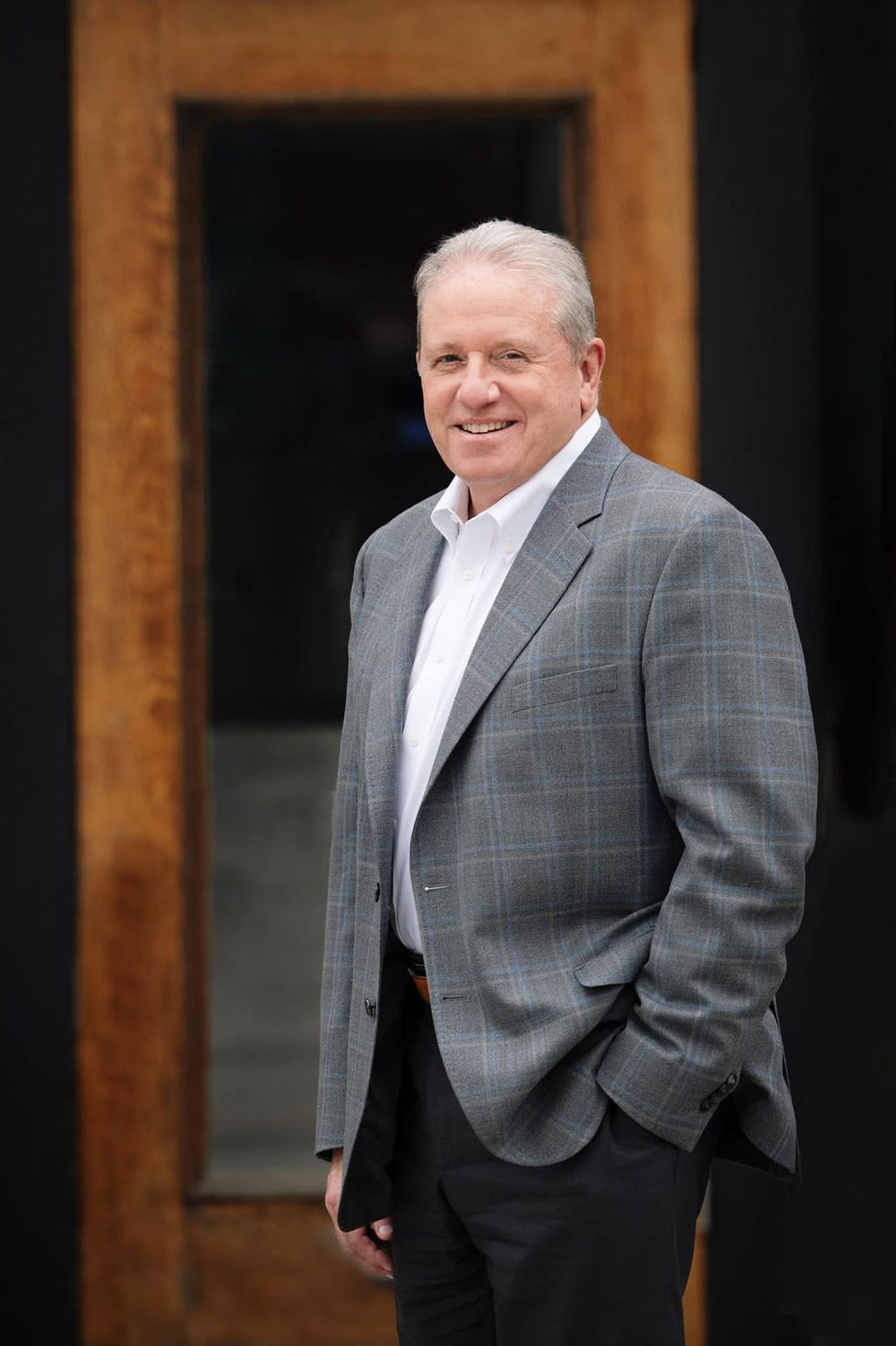 Professional wearing a gray plaid blazer and white shirt poses against wooden pillars in a sequence of casual shots.