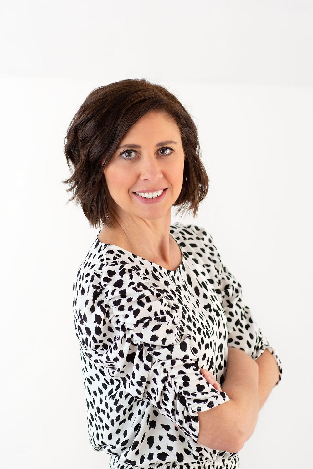 Professional portrait of someone wearing a black and white spotted blouse against a white background, with short dark hair.