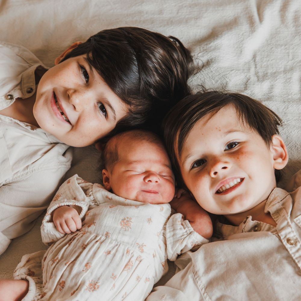 3 siblings together lying on bed with heads touching.